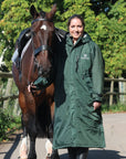 EQUIDRY women's long waterproof horse riding coat in black forest green/cream modelled by rider walking with horse