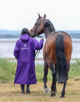 EQUIDRY women's long waterproof horse riding coat in deep purple/grey modelled by rider walking with horse