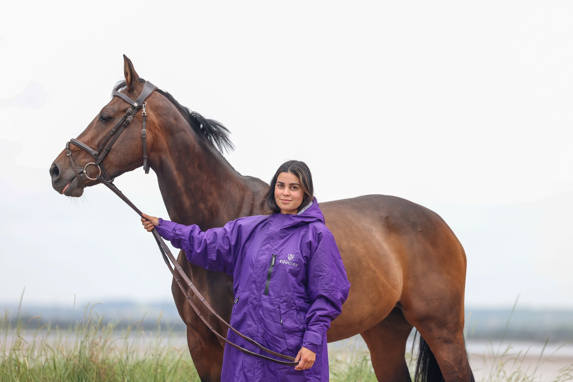 EQUIDRY women's long waterproof horse riding coat in deep purple/grey modelled by rider holding horse