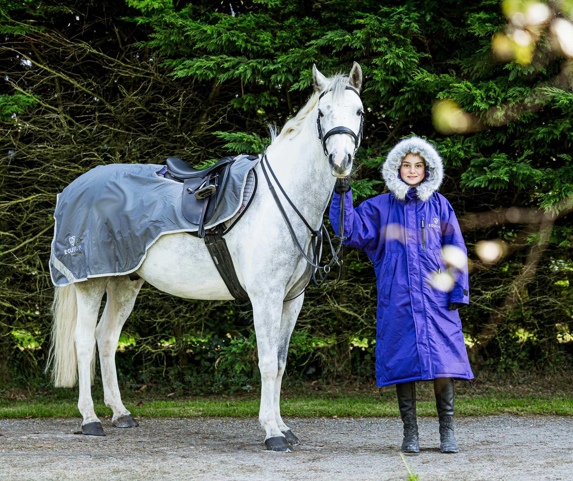 EQUIDRY Evolution Lux children's Warm Waterproof Winter Horse Riding Coat Thick Fleece Lining with Faux Fur Trim Hood being shown in purple by rider with horse in exercise sheet