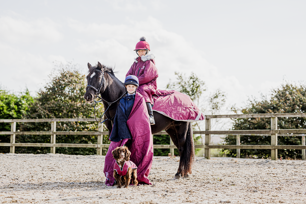 EQUIDRY Evolution Lux children's Warm Waterproof Winter Horse Riding Coat Thick Fleece Lining with Faux Fur Trim Hood being shown in plum with horse and dog