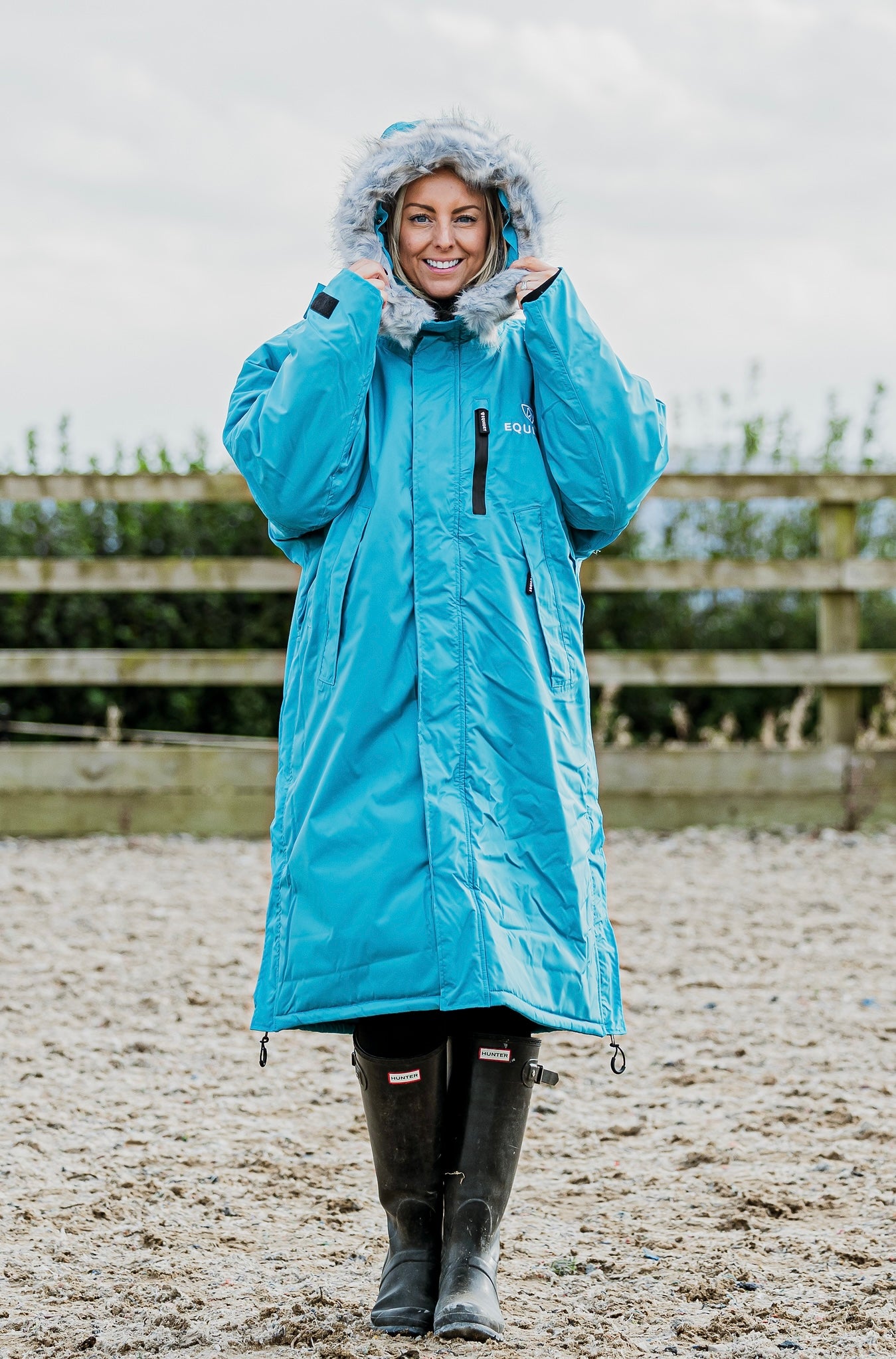 EQUIDRY Evolution Lux Women's Warm Waterproof Winter Horse Riding Coat Thick Fleece Lining with Faux Fur Trim Hood in turquoise rider stood with hood up