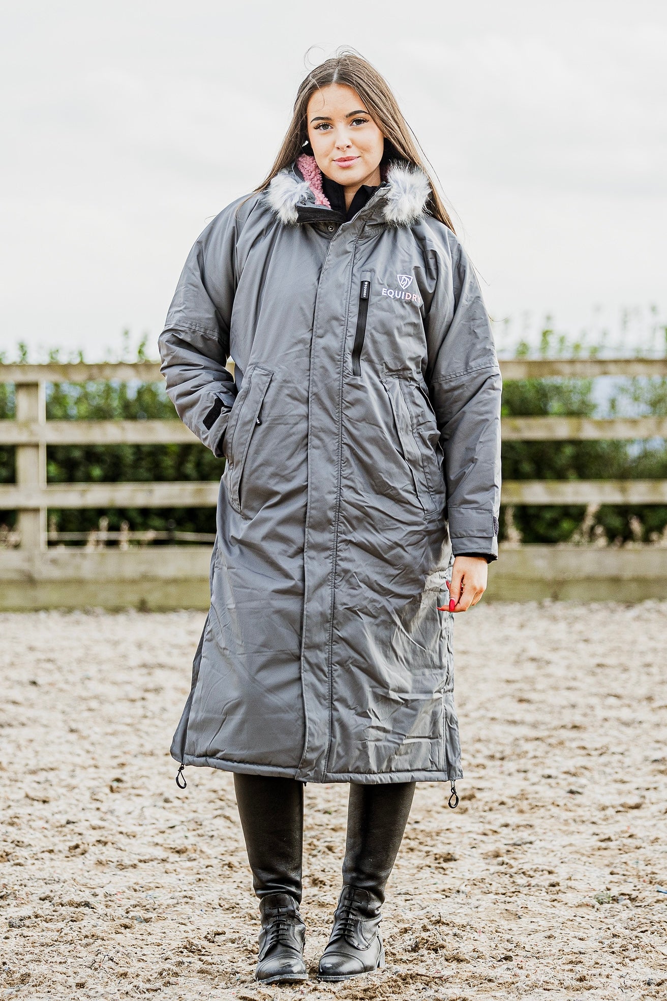 EQUIDRY Evolution Lux Women's Warm Waterproof Winter Horse Riding Coat Thick Fleece Lining with Faux Fur Trim Hood charcoal/pale pink modelled by rider in arena, full front view of coat