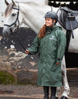 EQUIDRY women's thin fleece stowaway hood long waterproof horse riding coat in black forest green stood with horse