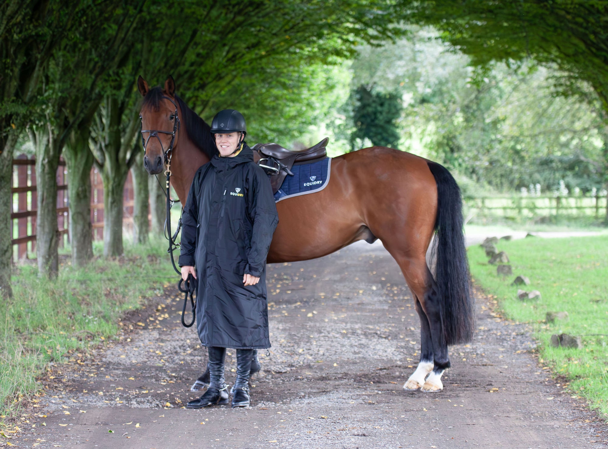  EQUIDRY men's long waterproof horse riding coat in Black/Yellow being modelled by male rider holding horse