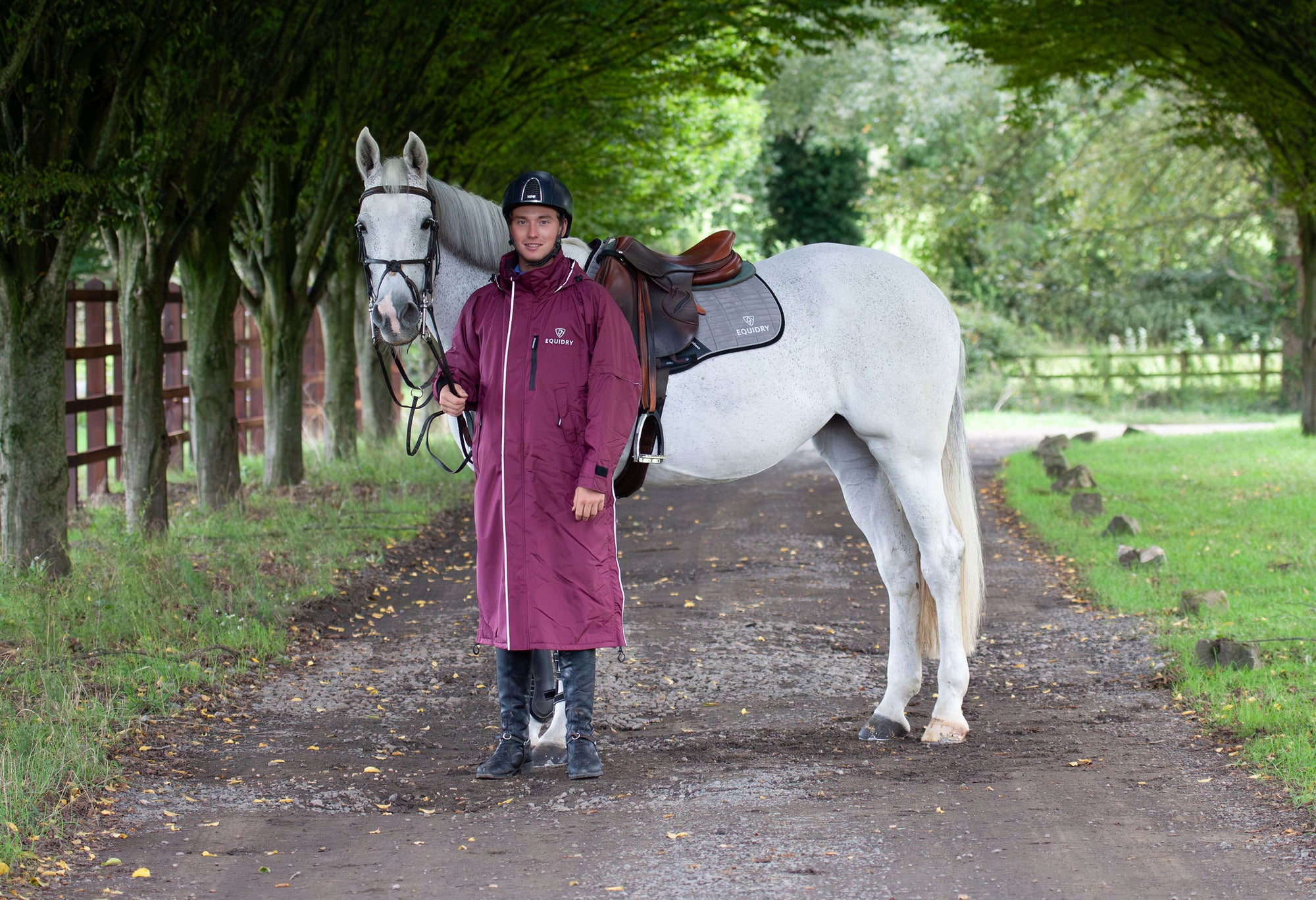 Evolution Reflective Men's Lightweight Waterproof Horse Riding Coat in plum worn by male rider stood with horse