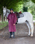 Evolution Reflective Men's Lightweight Waterproof Horse Riding Coat in plum worn by male rider stood with horse