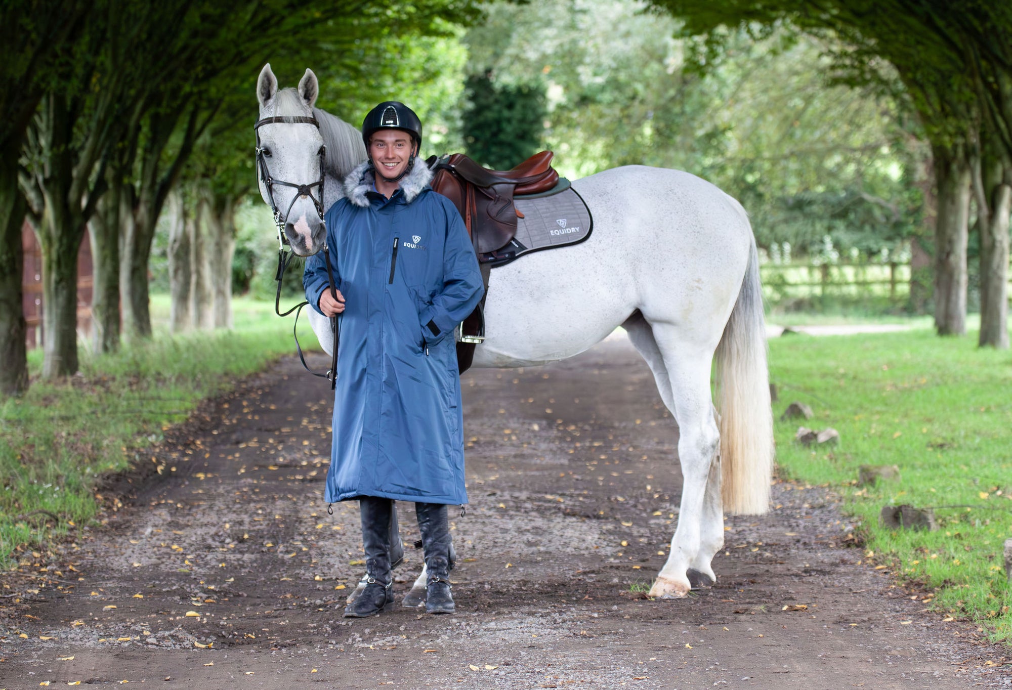 Evolution Lux Men's Warm Waterproof Horse Riding Coat in steel blue worn by male rider stood with horse 