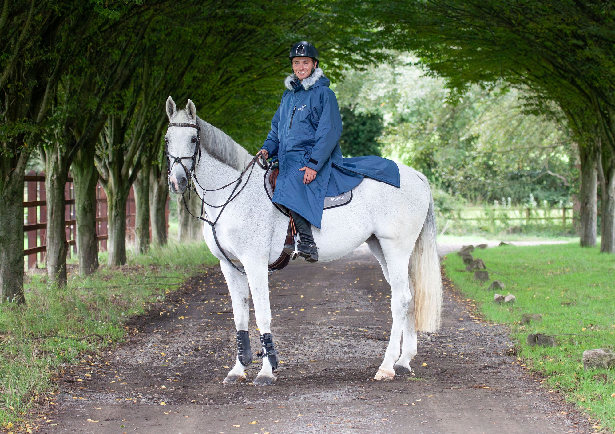 Evolution Lux Men's Warm Waterproof Horse Riding Coat in steel blue modelled by male rider on horseback showing storm skirts and side zips