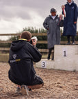 EQUIDRY women's long waterproof horse riding coat in Black/Yellow being used by photographer at show 