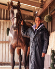 EQUIDRY women's long waterproof horse riding coat in Black/Lilac rider on yard with horse