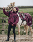 Shortie Child's Oversized Short Waterproof Riding Jacket Thin Fleece Lining Stowaway Hood in plum worn by rider with matching exercise sheet